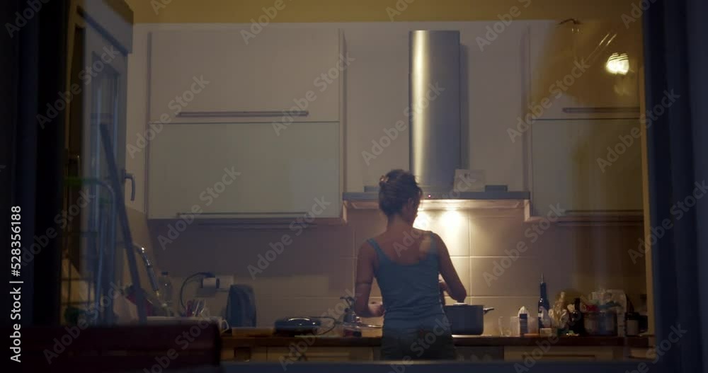 Rear view of a woman cooking in the kitchen at night. Rear view of a woman cooking in the kitchen at night.