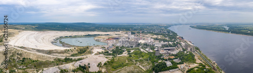 Panoramic aerial view of Cement Plant on Volga river bank on cloudy summer day. Volsk town, Saratov Oblast, Russia.