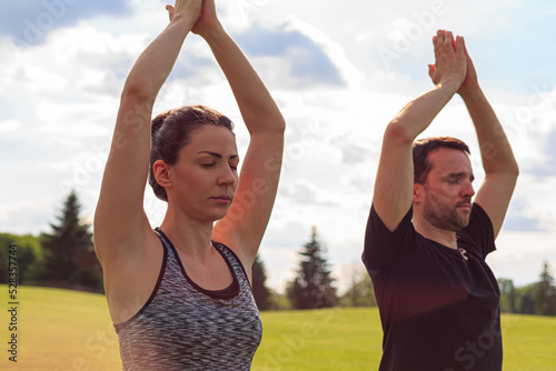 Close up of healthy man and woman doing yoga in the sunny summer park. Fitness and healthy lifestyle