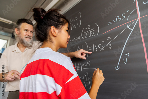 Fotografía Mature caucasian male high school maths teacher explains blackboard exercise to asian girl teen student