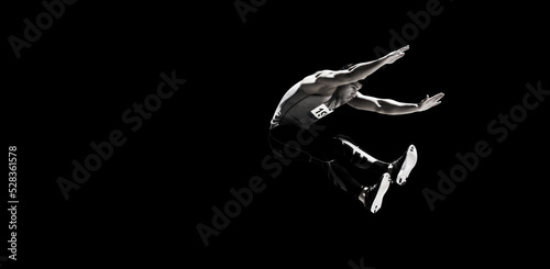 Sportsman long jumping against black background