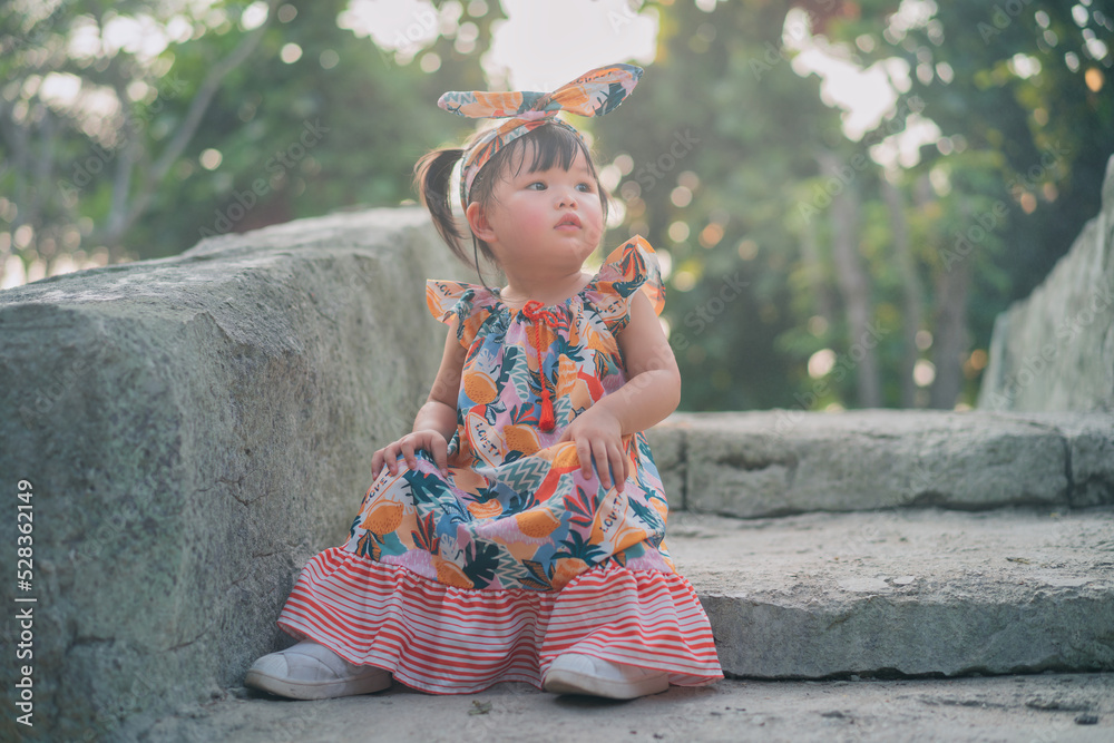 Asian Japnese baby sit on stone stairs in the park. 1 year 6 month baby play in the park use as concept of play, summer, health, mood and motion of baby and kid development.