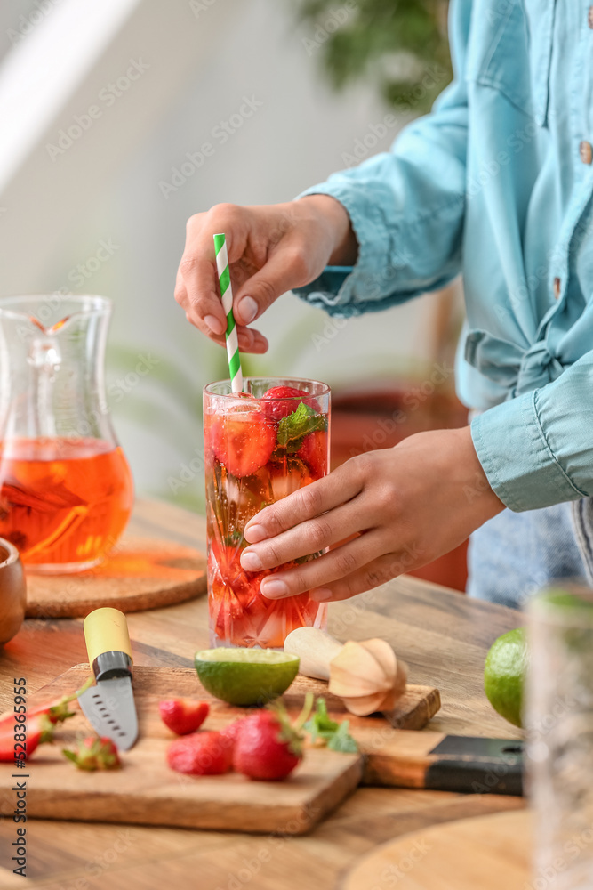 Woman with glass of tasty cold strawberry lemonade in kitchen Woman with glass of tasty cold strawberry lemonade in kitchen