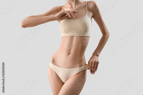 Slim young woman in underwear on light background