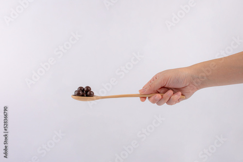 Hand and chocolate balls on wooden spoon on a white background.