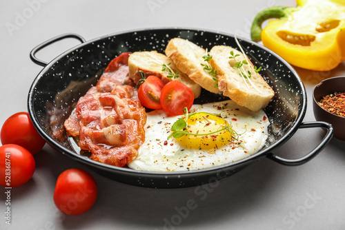 Frying pan with tasty fried egg, bacon and bread on grey background, closeup