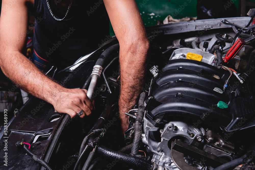 High quality photography. An unrecognizable mechanic reaching into the engine of a car he is repairing. Mechanic checking engine of a car to find the problem. High quality photography. An unrecognizable mechanic reaching into the engine of a car he is repairing. Mechanic checking engine of a car to find the problem.
