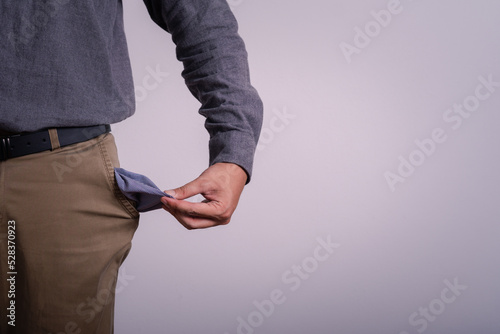 Poor businessman hand holding and showing his empty pocket money with gray background copy space fortext.