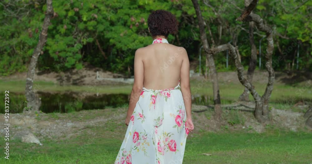 Sexy light skin girl walks toward a lake in the park before turing around with her dress flowing in the wind Sexy light skin girl walks toward a lake in the park before turing around with her dress flowing in the wind