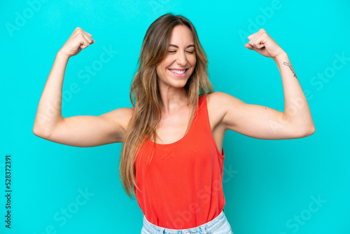 Young caucasian woman isolated on blue background doing strong gesture