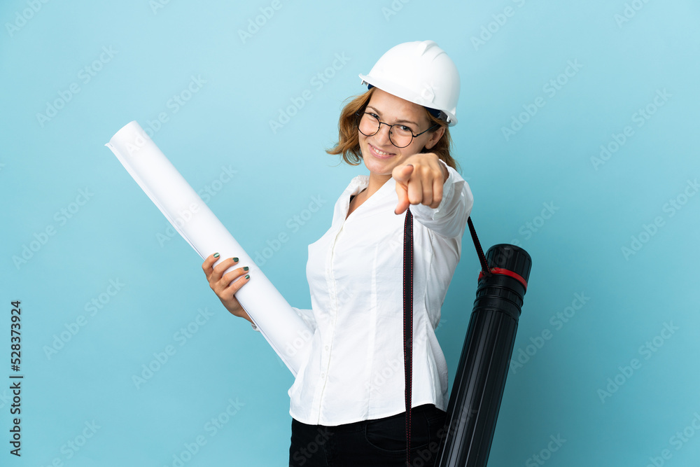 Young architect Georgian woman with helmet and holding blueprints over isolated background pointing front with happy expression Young architect Georgian woman with helmet and holding blueprints over isolated background pointing front with happy expression