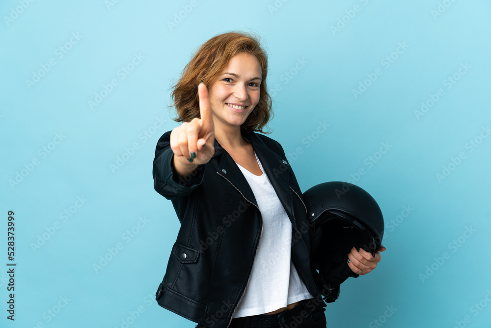 Georgian girl holding a motorcycle helmet isolated on blue background showing and lifting a finger