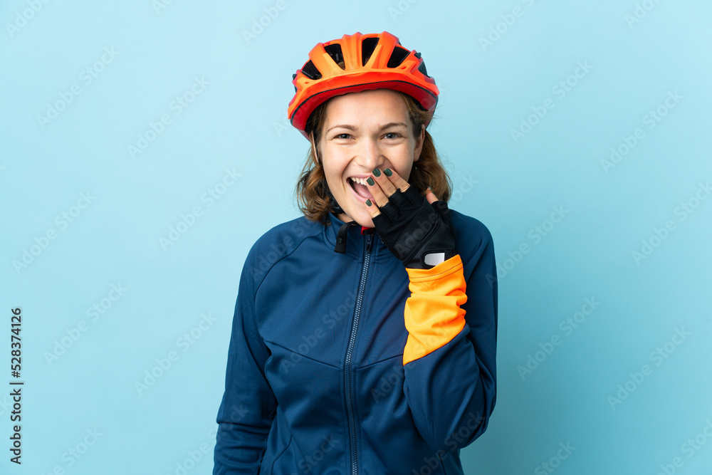 Young cyclist woman isolated on blue background happy and smiling covering mouth with hand Young cyclist woman isolated on blue background happy and smiling covering mouth with hand