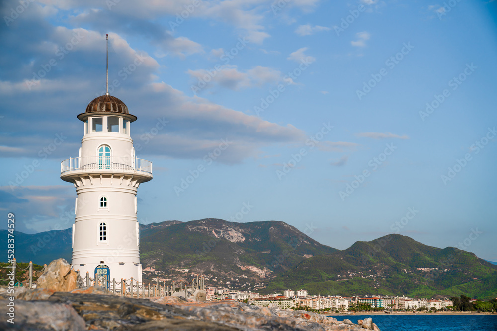 White port lighthouse on the background of mountains and sky and sea. Copy space