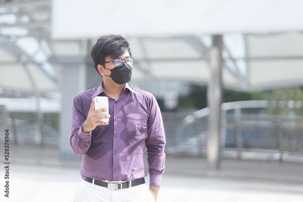Fototapeta premium Sweating asian business man wearing face mask using mobile phone during office hours as part of Business New Normal