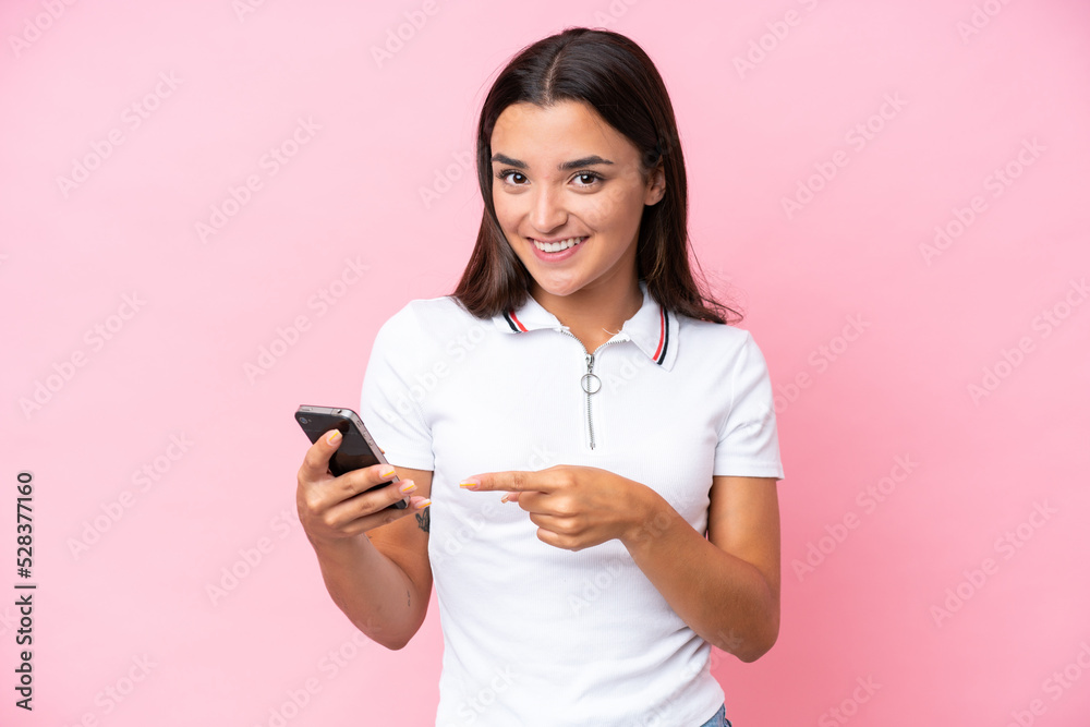Young caucasian woman isolated on pink background using mobile phone and pointing it Young caucasian woman isolated on pink background using mobile phone and pointing it