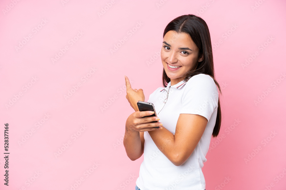 Young caucasian woman isolated on pink background using mobile phone and pointing back Young caucasian woman isolated on pink background using mobile phone and pointing back