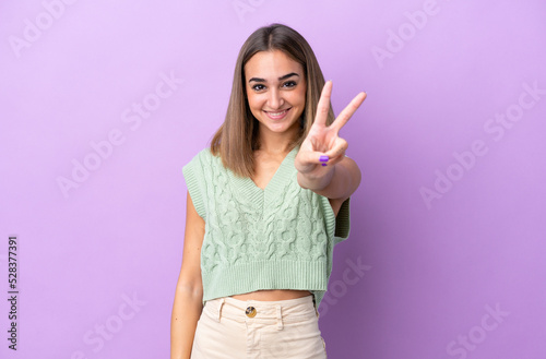 Young caucasian woman isolated on purple background smiling and showing victory sign