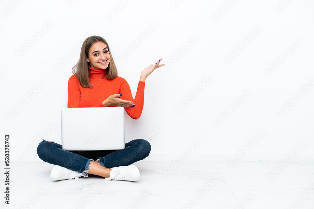 Young caucasian woman sitting on the floor with a laptop extending hands to the side for inviting to come Young caucasian woman sitting on the floor with a laptop extending hands to the side for inviting to come