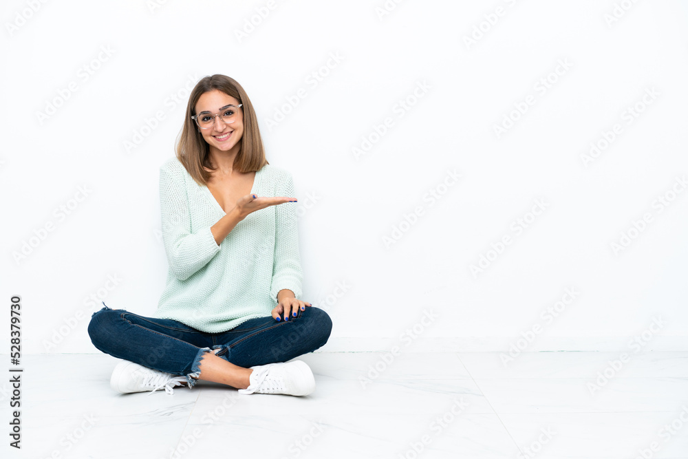 Young caucasian woman sitting on the floor isolated on white background presenting an idea while looking smiling towards Young caucasian woman sitting on the floor isolated on white background presenting an idea while looking smiling towards