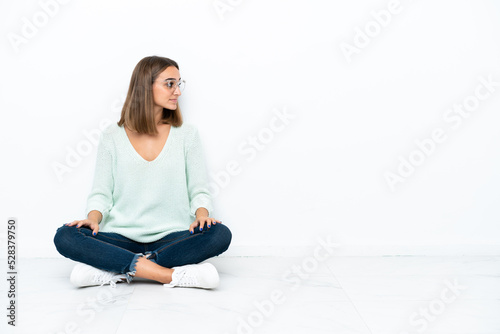 Young caucasian woman sitting on the floor isolated on white background in lateral position