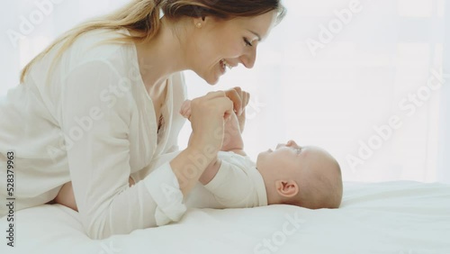 Happy mom spends time with her newborn baby. Mother playing and kissing with a newborn baby. Face of an active baby looking at a parent. Motherhood and family concept photo