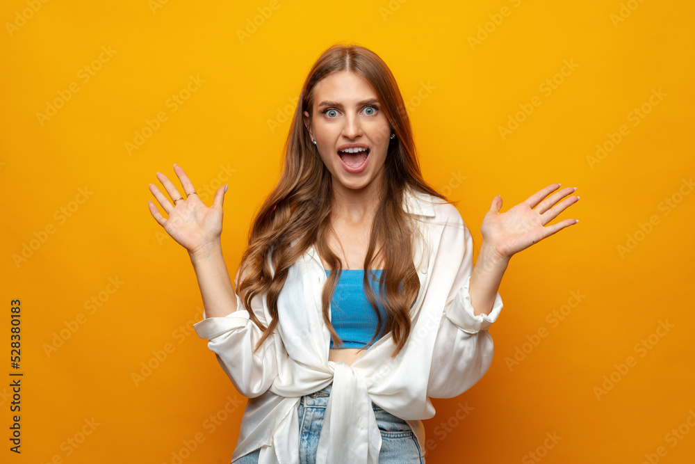 Young pretty surprised smiling woman standing with open palms on yellow background Young pretty surprised smiling woman standing with open palms on yellow background
