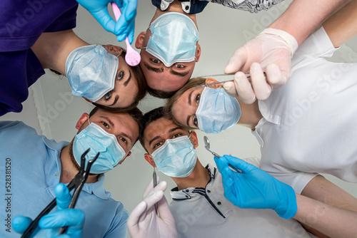 group of doctors standing in a circle with medical instruments all looking down on patient