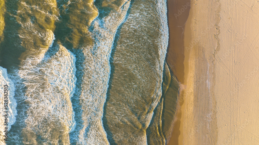 Fototapeta premium An aerial view of the wide beach and waves. Seascape from a drone during sunset. A sandy seashore. The sea and the shore. View of the beach from above.