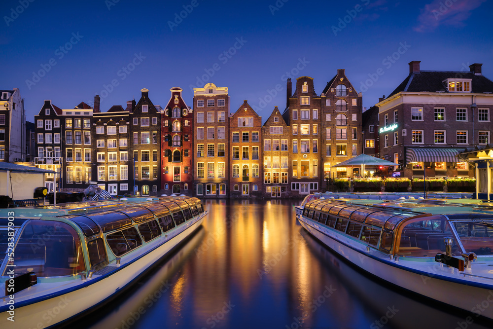 Damrak, Amsterdam, Netherlands. View of houses and boats during sunset. The famous Dutch canals and boats. A cityscape in the evening. Travel photography.