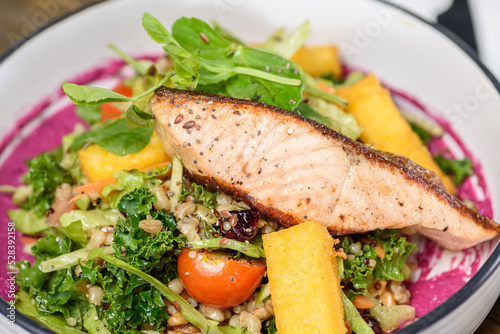 A seafood dinner or lunch with a piece of grilled Salmon on a bed of healthy vegetables and salad, in a round white bowl