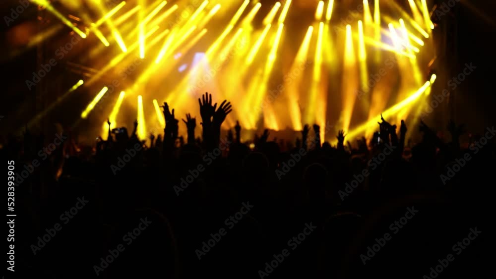 Hands up silhouettes of exited fans at night concert, bright neon stage with golden lights, slow motion Hands up silhouettes of exited fans at night concert, bright neon stage with golden lights, slow motion