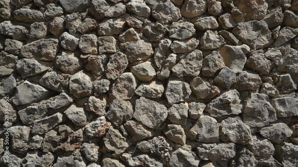 Left pan - Crude, unworked rock wall with visible concrete among the stones. Shadows and sunlight.Natural stone is a forward thinking material for the construction industry. Left pan - Crude, unworked rock wall with visible concrete among the stones. Shadows and sunlight.Natural stone is a forward thinking material for the construction industry.