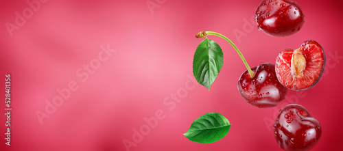 red cherries and slice with water drops flying in the air stream on pink background