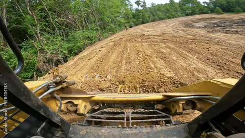POV while operating a skid steer loader to smooth dirt at a land development site; operators hands, loader controls and bucket with linkages are visible photo