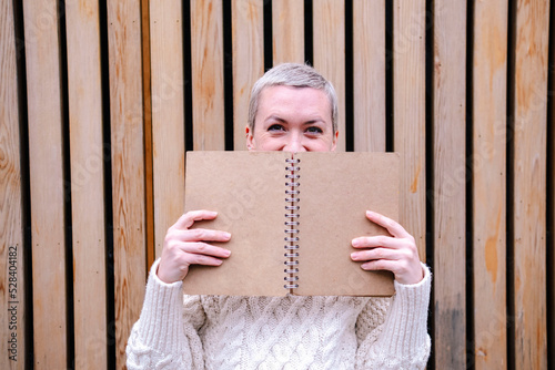 Woman hiding face behind open book in front of wall photo