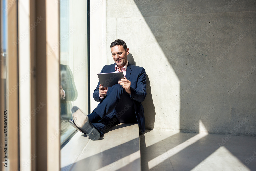 Smiling businessman using tablet PC sitting in office Smiling businessman using tablet PC sitting in office