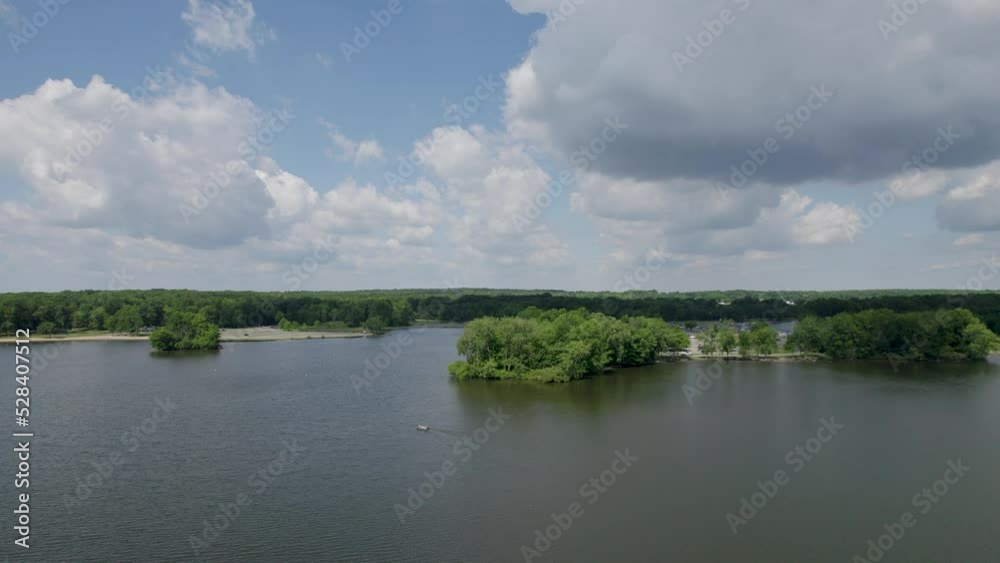 A drone shot of beautiful lake reservoir with thick forest against white clouds in blue sky. A beautiful nature's view is seen A drone shot of beautiful lake reservoir with thick forest against white clouds in blue sky. A beautiful nature's view is seen