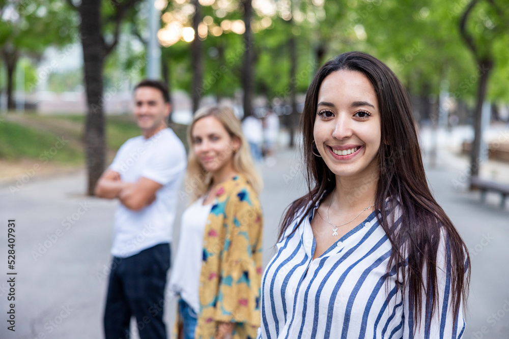 Smiling young woman with long hair standing in front of friends at park Smiling young woman with long hair standing in front of friends at park