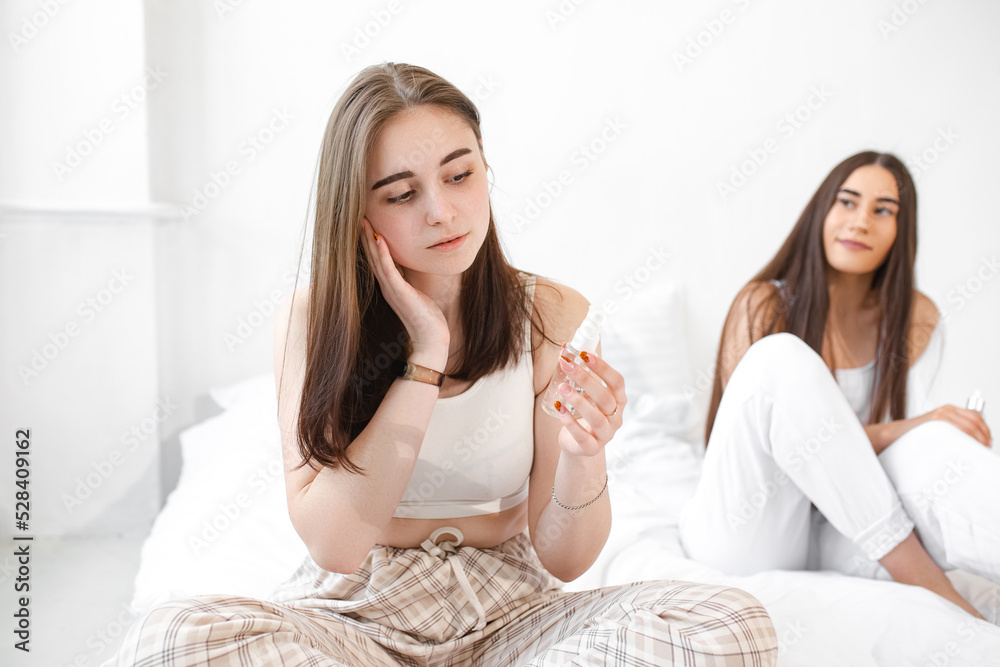 Two young beautiful girls with cosmetics. Women make face masks to take care of their skin. Girlfriends in a home spa rest and relax on a white bed Two young beautiful girls with cosmetics. Women make face masks to take care of their skin. Girlfriends in a home spa rest and relax on a white bed