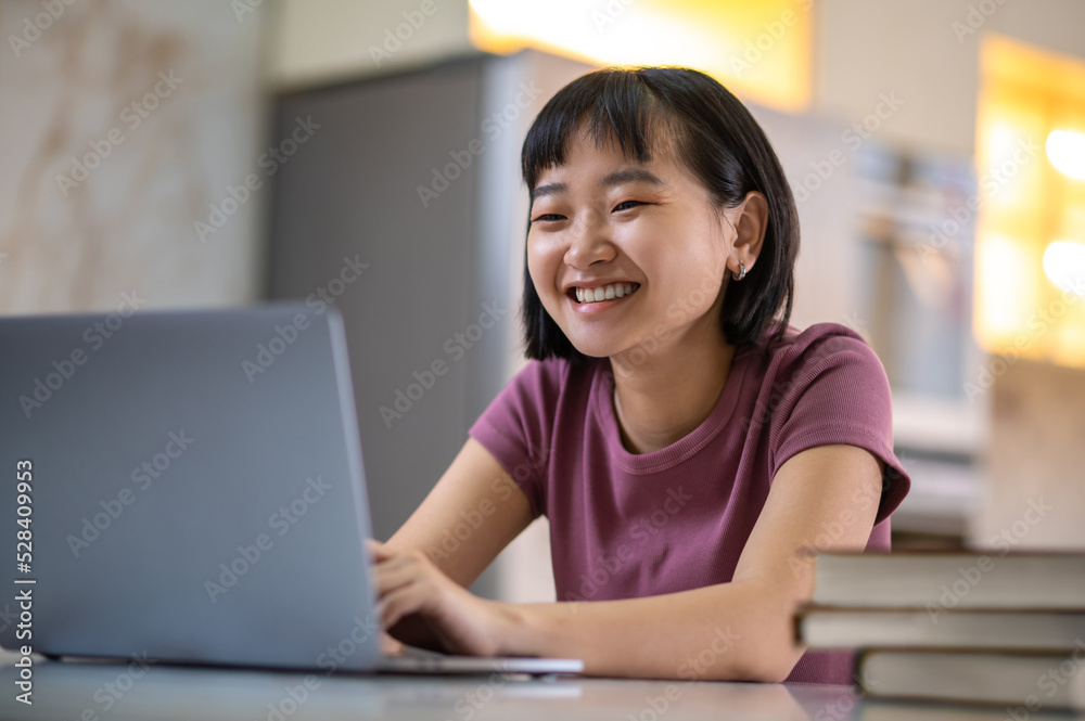 A girl in violet tshirt sitting at the laptop and looking happy A girl in violet tshirt sitting at the laptop and looking happy