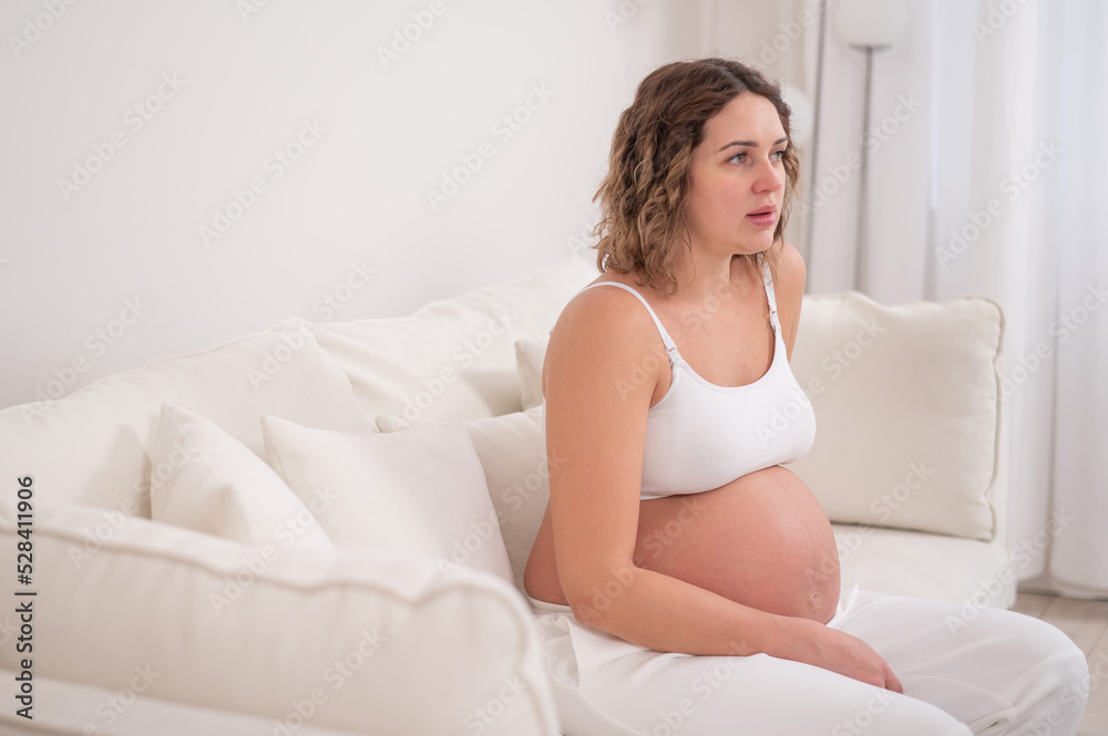 Tired pregnant woman sits on a white sofa. Tired pregnant woman sits on a white sofa.
