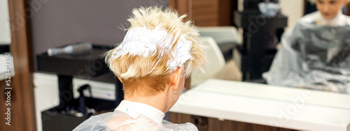 Coloring white hair with hair dye of the young caucasian blonde woman sitting at a hair salon, close up photo