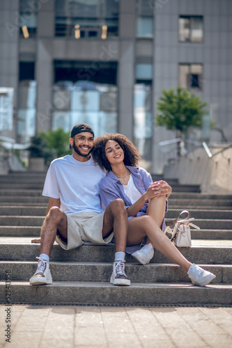 Young cute couple sitting on the steps and looking peaceful and happy
