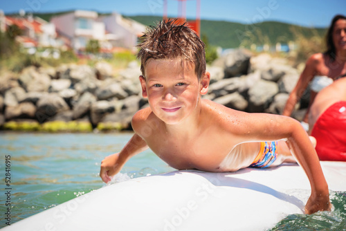 Cheerful teenage boy lying on a swimming board. Happy european family having fun floating on a swim board in the sea on a hot summer day