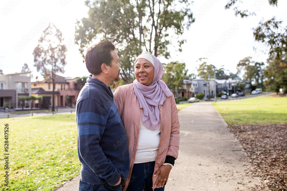 middle aged woman wearing pink hijab and smiling middle aged man looking at each other on a big lawn middle aged woman wearing pink hijab and smiling middle aged man looking at each other on a big lawn
