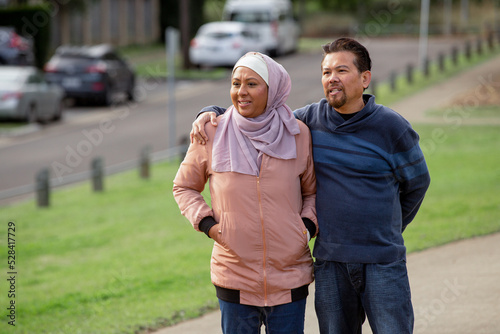 middle aged woman wearing pink hijab and middle aged man wearing blue sweater putting his arm on her photo