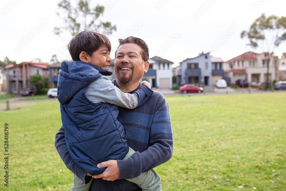 smiling middle aged man wearing blue sweatshirt carrying a smiling boy in his arms on a big lawn smiling middle aged man wearing blue sweatshirt carrying a smiling boy in his arms on a big lawn