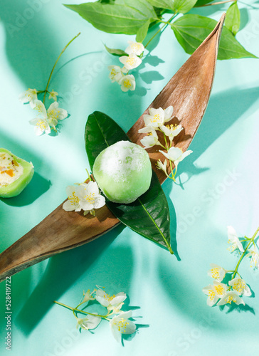 Green mochi on a wooden stand, decorated with fresh jasmine flowers. On a green background.