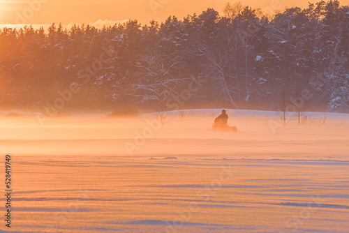 Amazing winter sunset in the forest with the orange sky, and snowmobile driving in the mist © MKozloff